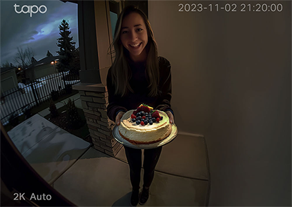 Woman on doorstep at night holding a birthday cake.
