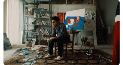 still image of man sitting in painters studio holding a brush and block