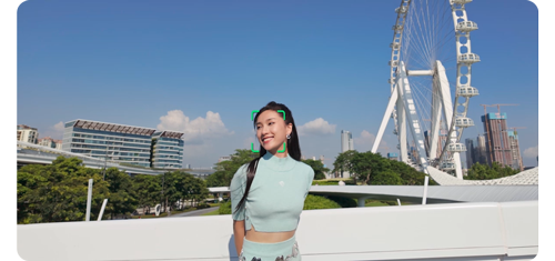 photograph of a woman wearing light blue clothing in front of a large modern bridge and ferris wheel with face tracking markers
