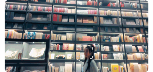 woman walking in front of library display cases with face auto-detect tracking