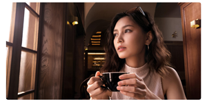 woman sat holding a black cup of coffee infront of a window