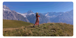 woman wearing a red flowery dress walking along an alpine hill looking across mountain tops