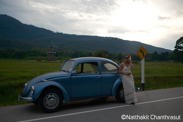 Fujifilm XT5 Nostalgic Negative Film Simulation sample image a woman in a long dress leaning against a classic VW Beetle at the side of a road with grean fields behind