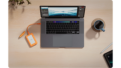 LaCie Rugged Mini SSD sat on table connected to Macbook Pro with coffed cup to the side