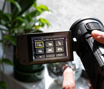 person holding panasonic camcorder with video editing menu open on screen