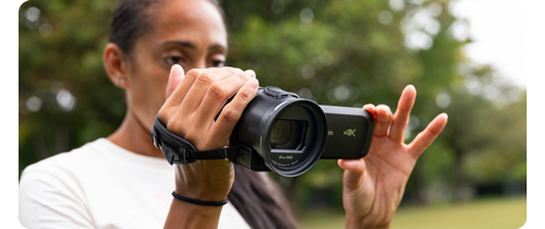 Person holding Panasonic HC-V900 HD Camcorder recording video while standing in tree lined park