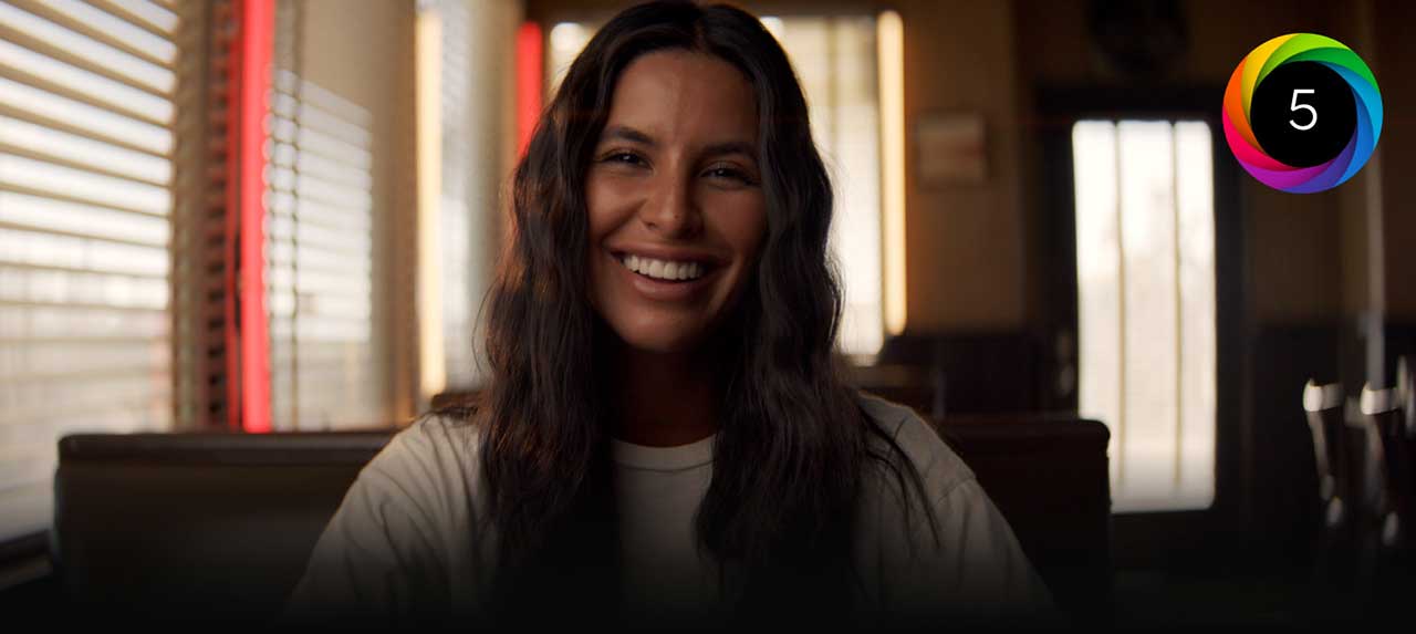portrait of a woman sat smiling in a diner booth with the blackmagic generation 5 colour science logo overlayed, blackmagic cinema camera 6k