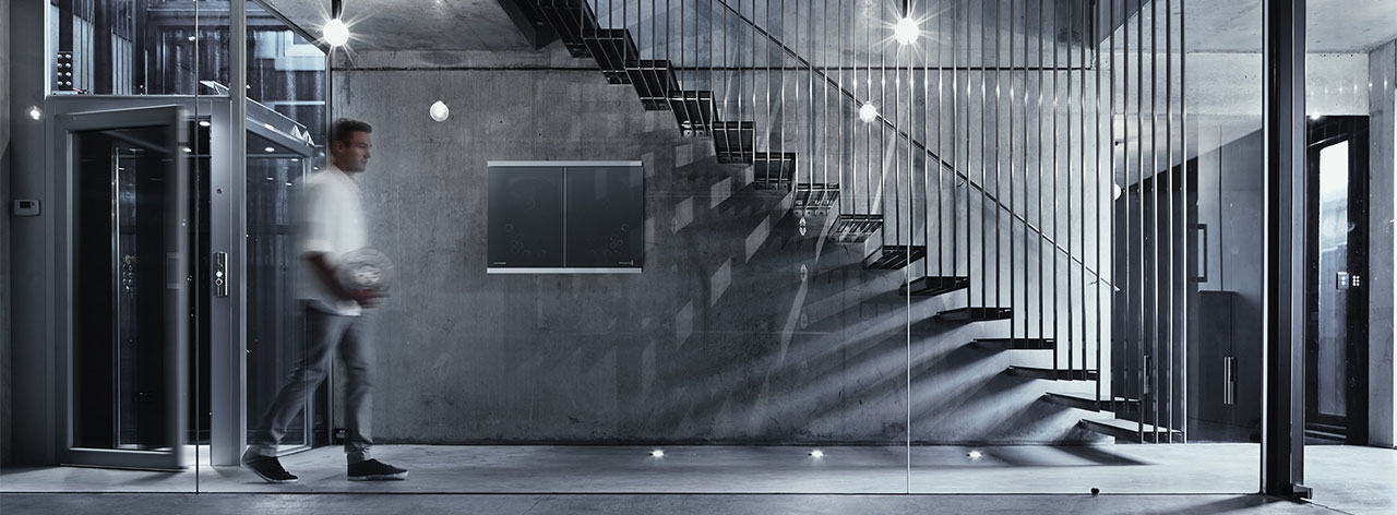 man walking past Cintel G3 HDR+ scanner mounted to concrete wall below metal stairs