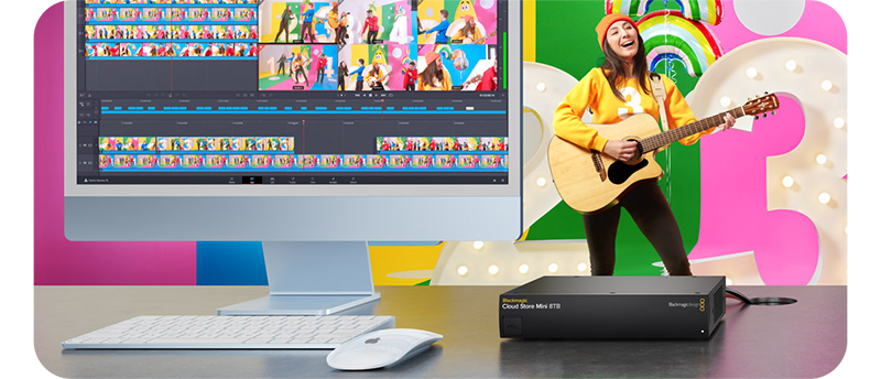 Blackmagic Cloud Store Mini on desk with Apple Mac M1 with woman playing guitar infront of bright coloured backdrop