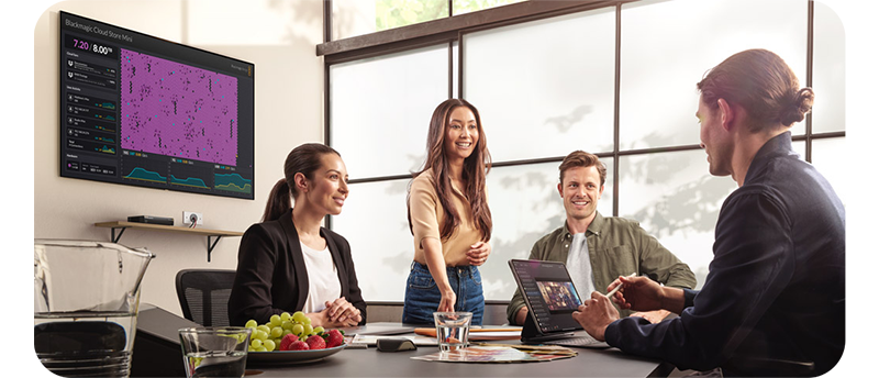 four people sat around a meeting table with Blackmagic Cloud real time monitoring display on meeting room wall
