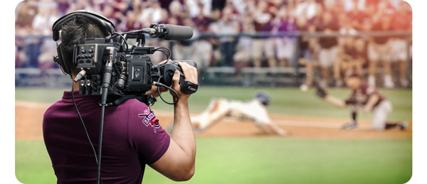 man with URSA Broadcast looking towards a baseball game where the runner is diving for third base