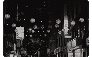 high contrast black and white photograph of paper lanterns hanging above tokyo stree at night time
