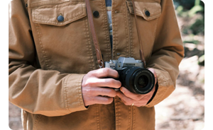 close up image of photographer holding Fujifilm X-T50 against body wearing tan chore jacket