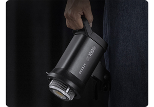 Person holding Godox SL100Bi light against dark background