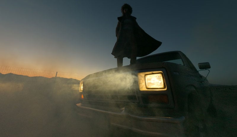 low-light sample image of someone stood on the hood of a truck in a long coat