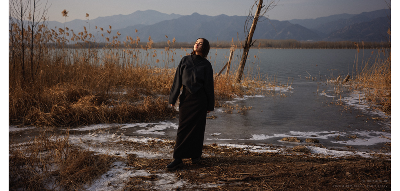 Hasselblad 907X 100C sample image portrait of brunette woman wearing all black standing in front of scenic lake with snow on the ground