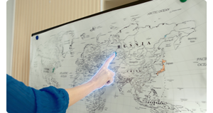 person pointing to russia on a world map with their hand outlined in blue
