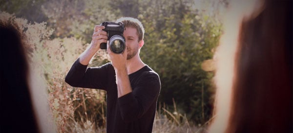 photographer holding camera standing in front of tree line