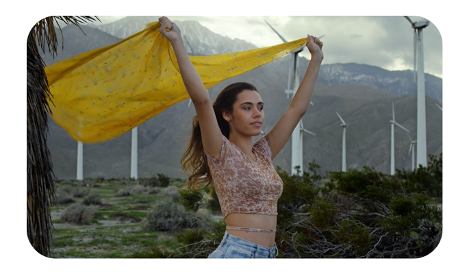woman holding yellow flag over head in front of a wind farm, samyang rokinon xeen meister lenses