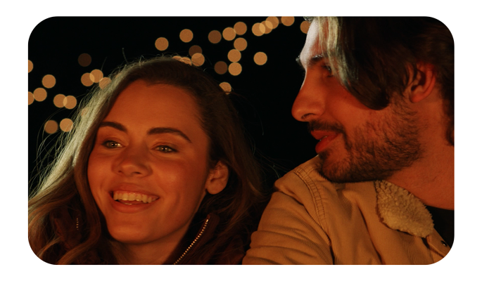 Couple sat in front of campfire at night, showcasing round bokeh in background