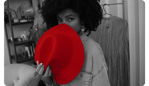 black and white photo with selective colour of a woman in front of her closet with a bright red hat