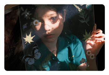 example portrait of a woman holding a piece of glass with flowers on in front of her face taken with the AF 56mm F1.8 APS-C camera lens