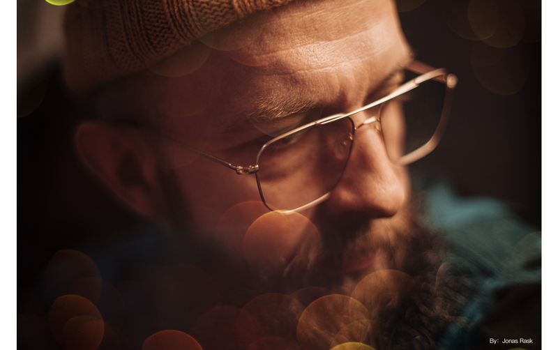 TTArtisan 35mm f0.95 sample photograph of man wearing square framed glasses and orange beanie under warm soft light with spherical bokeh front of frame