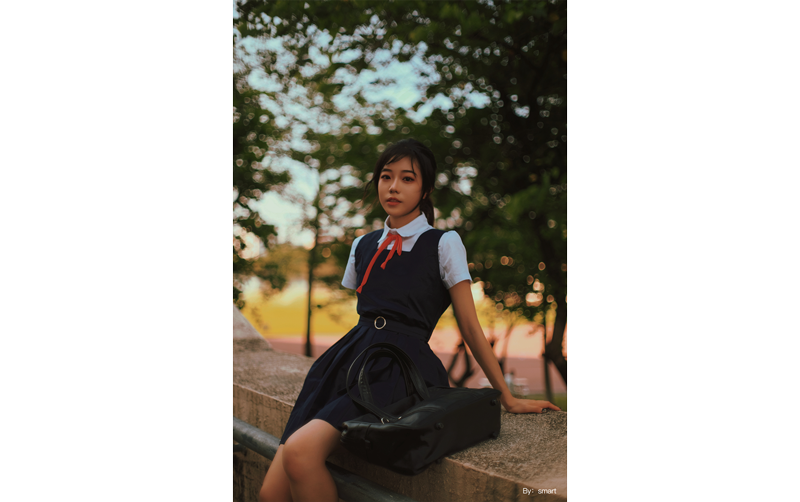 TTArtisan 35mm f0.95 sample photograph of asian model wearing uniform dress sitting on concrete park ledge new trees