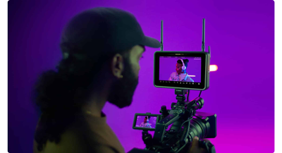 filmmaker using a camera righ with atomos display to capture an act on a purple set