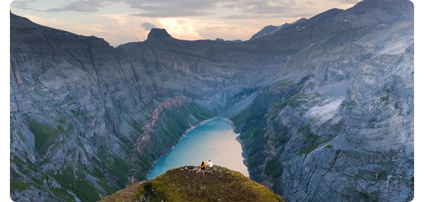 panorama photograph of nordic fjord with bright blue water and two people stood on top of a peak in the foreground