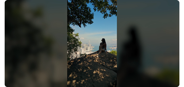 vertical photograph of a woman sat in the shade of a tree infront of a coastal city scape