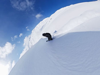 Snowboarder traveling down slope holding DJI Osmo 360