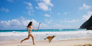 woman running along beautiful sunny beach with golden retreiver
