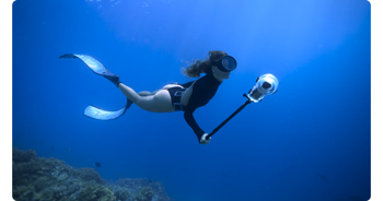 Female free diver holding Insta360 X5 in deep blue ocean