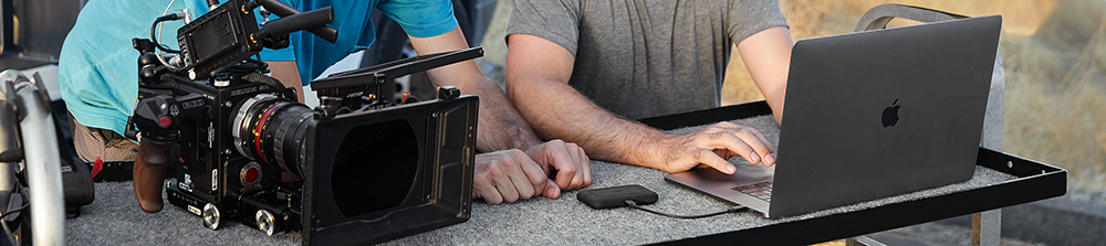 Filmmaker working on a macbook on a DIT cart with Camera and LaCie Rugged SSD Pro