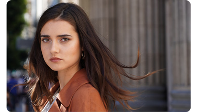 Sony E 16-55mm F2.8 G Lens Sample Image portrait of brunette haired woman wearing muted orange blazer standing infront of carved stone pillars