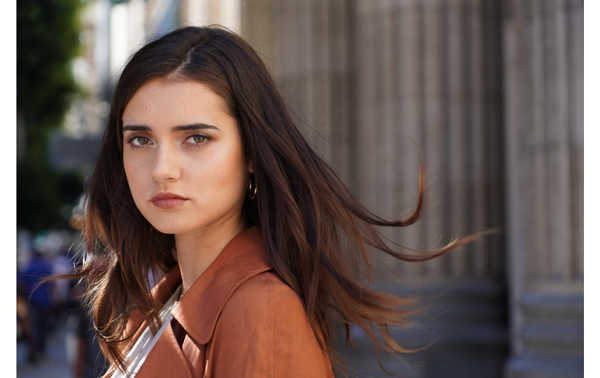 Sony E 16-55mm F2.8 G Lens Sample Image portrait of brunette haired woman wearing muted orange blazer standing infront of carved stone pillars