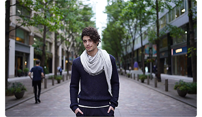 Sony FE 35mm F1.4 G Master Lens sample image of man wearing blue jumper and large silk scarf walking down a tree line street with retail stores
