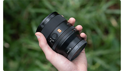Photographer holding Sony FE 35mm F1.4 G Master Lens in their hand above long green grass