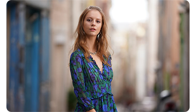 Sony FE 135mm F1.8 GM Lens sample image portrait of red haired woman wearing a blue and green floral dress standing in a long street