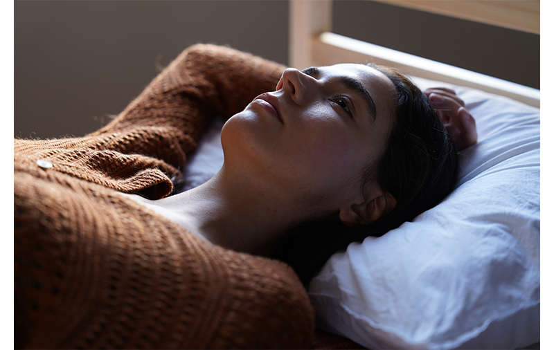 Sony FE 24-70mm F2.8 GM II Lens sample image close up of brunette woman lying on bed with white pillow wearing a muted orange jumper