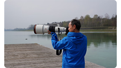 Photographer holding Sony FE 600mm F4 G Master OSS Lens and camera looking out over a lake from a jetty dock