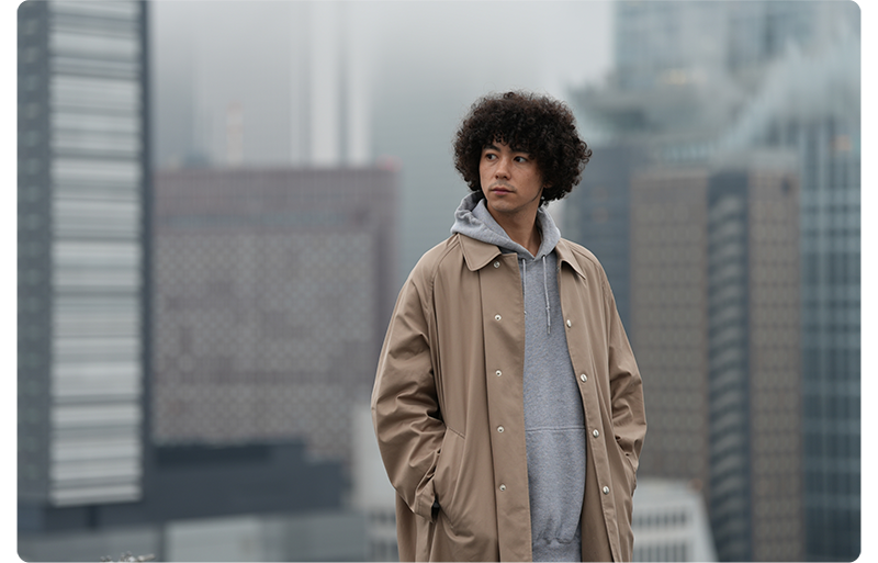 Sony FE 70-200mm F2.8 GM OSS II Lens sample image portrait of man wearing grey hoodie with tan raincoat and curly brown hair standing infront of city skyline background