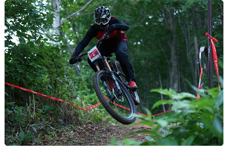 Sony FE 70-200mm F2.8 GM OSS II Lens sample image of downhill mountain bik rider jumping over a crest wearing black and red protective gear