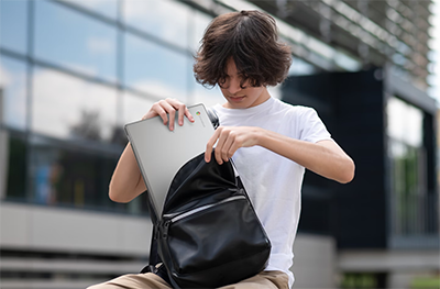 Image of a young man putting the laptop into his backpack.