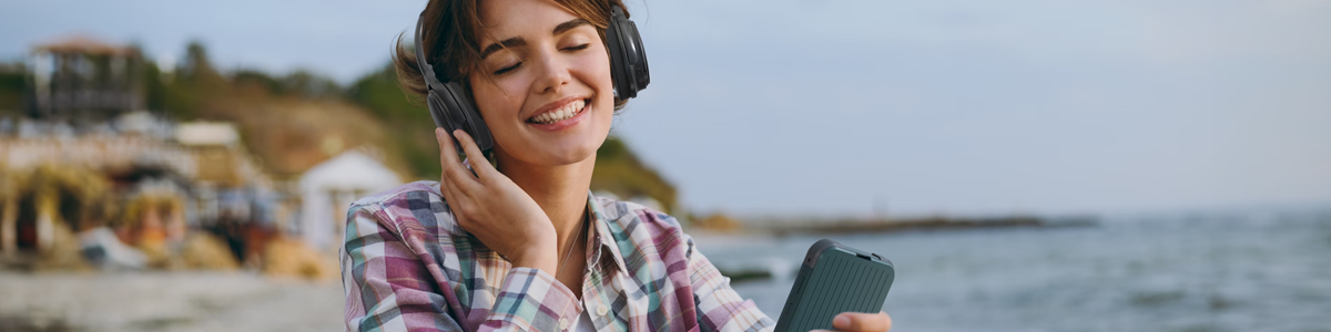 Woman with headphones at the seaside, using the Acer Connect M4 5G mobile hotspot to stream her music