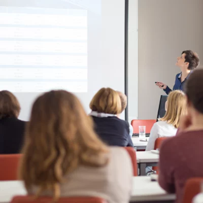 Teacher delivering lesson to children in classroom focussing on projector screen.