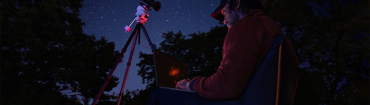 Man sat in the wilderness using his MacBook Pro, overlooking a starlit sky.