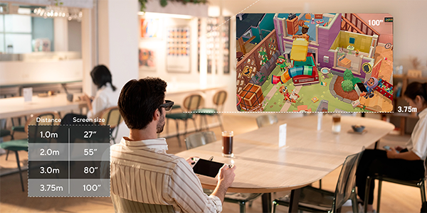 Man wearing ASUS AirVision M1 glasses, sat in dining area, playing ROG Ally with illustration of game beside him, highlighting upto 100-inch screen size.