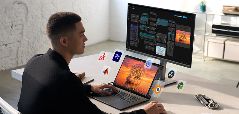 Man sat at desk, multitasking between laptop and monitor with software icons surrounding the laptop screen.